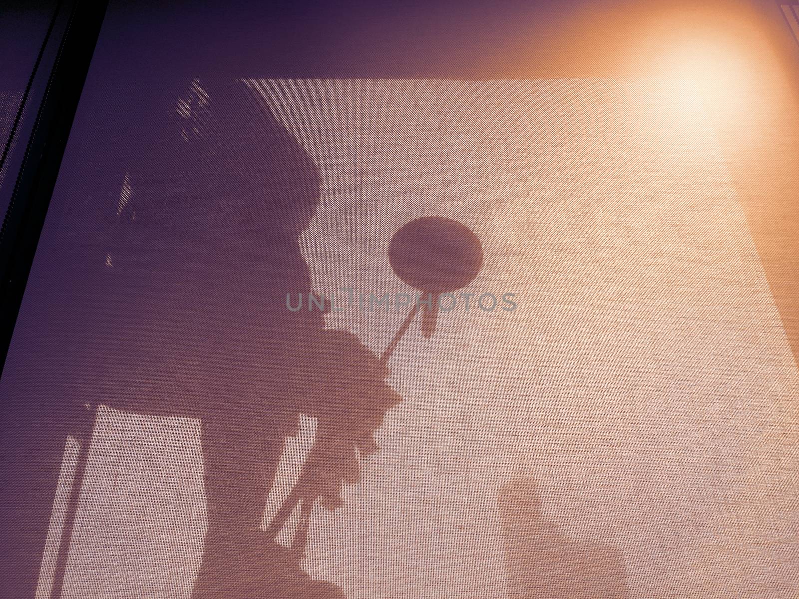 Silhouette images and shoot through transperent curtain effect from inside building which a man cleaning the window of high office building with his equipment such as wipe, sponge, bucket and high risk of danger