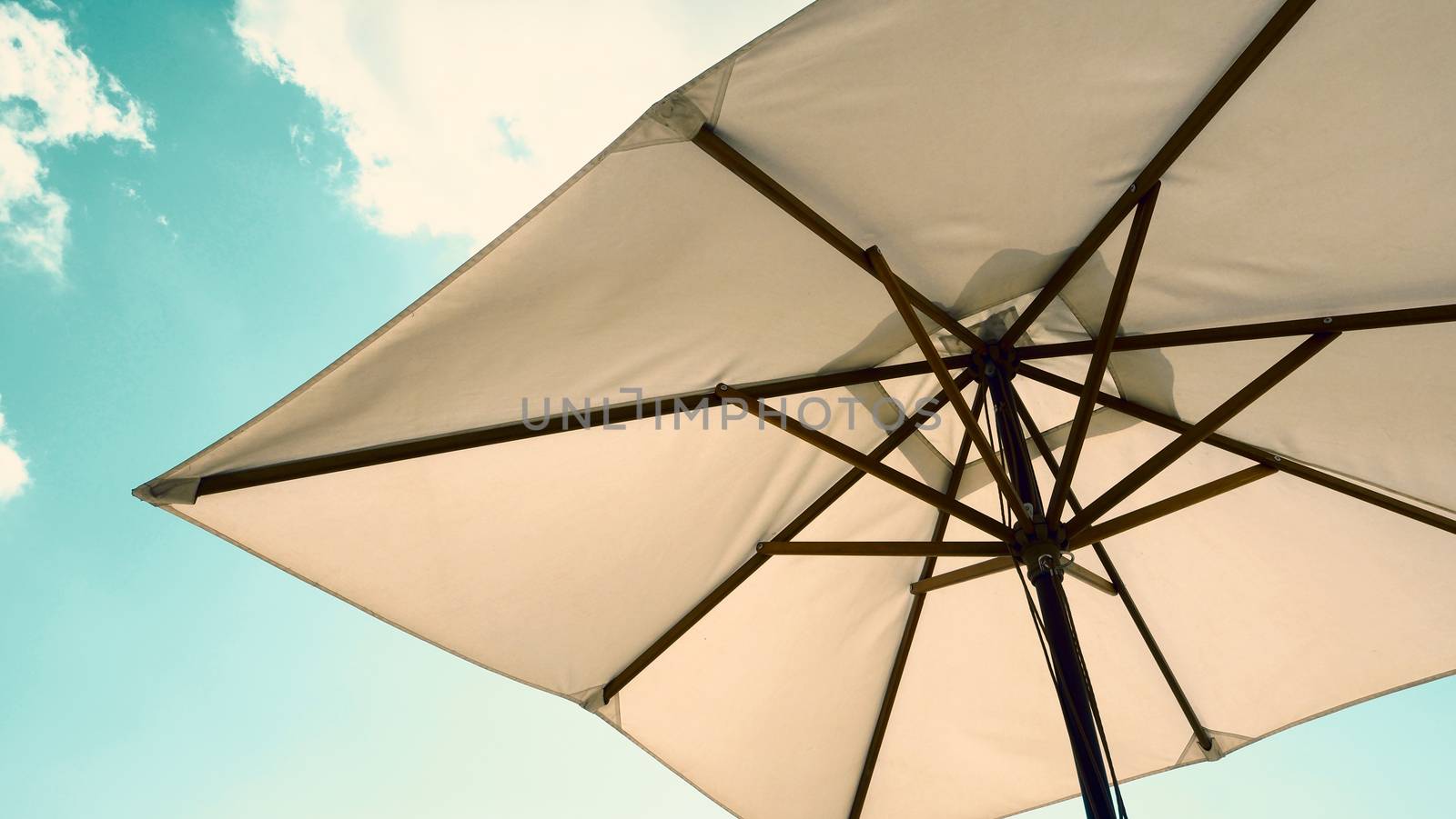 White fabric color texture beach umbrella and brown wood tripod with white cloud and clear blue sky summer sunlight day in low angle view camera for travel asia Thailand Pattaya.