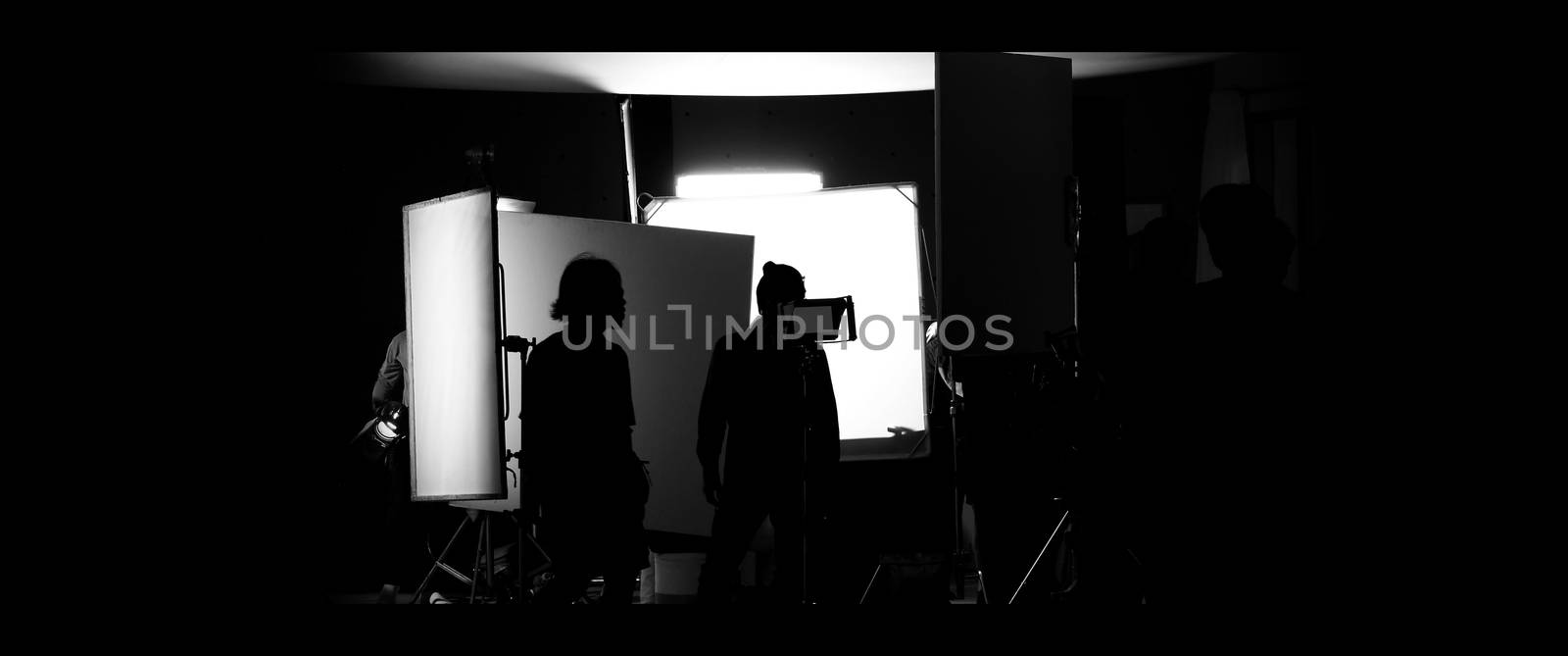 Shooting studio behind the scenes in silhouette images which film crew team working for filming movie or video with professional lighting and equipment such as camera, tripod, soft box, monitor