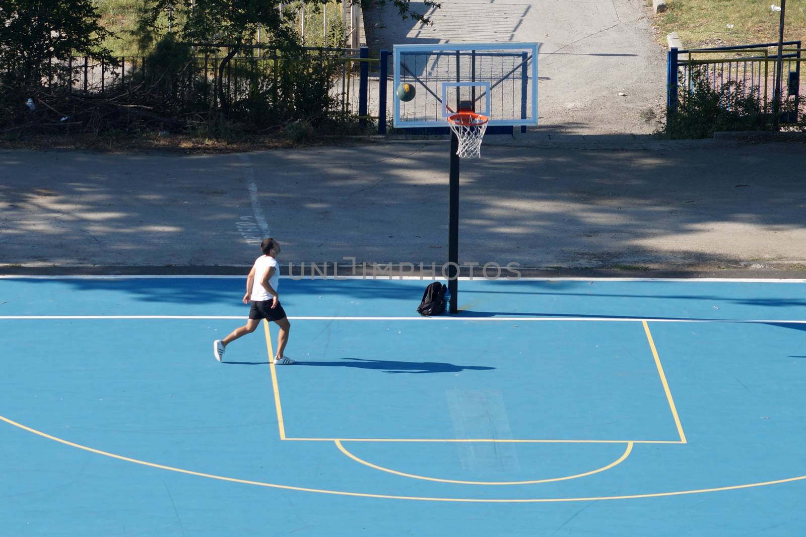 Varna, Bulgaria - August, 22, 2020: young man training with a ball on an outdoor basketball court