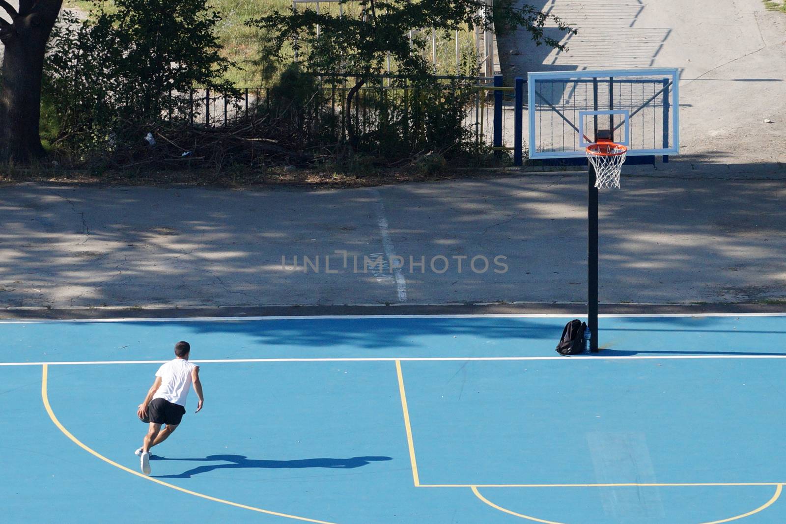 young man training with a ball on an outdoor basketball court by Annado