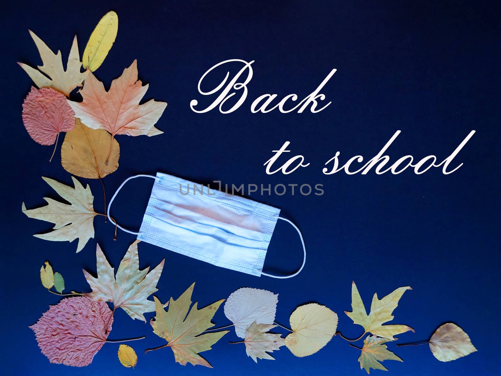 medical mask and autumn leaves on blue background text back to school