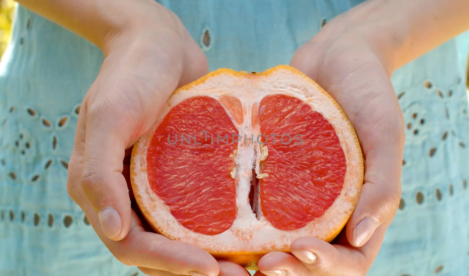 Close up red grapefruit half in female hands. Healthy fresh food concept