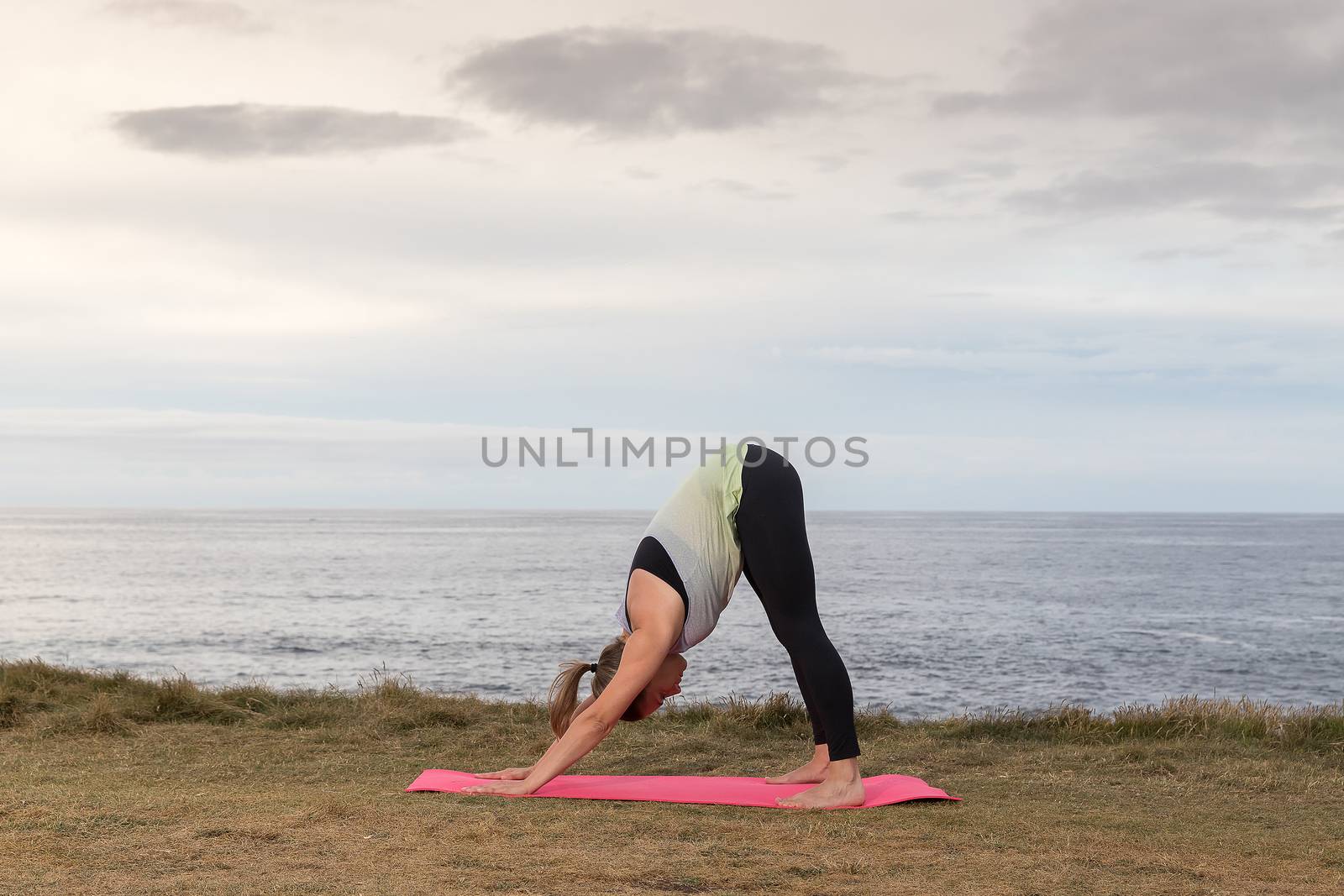 Woman doing yoga outdoors with the sea in the background. by JRPazos