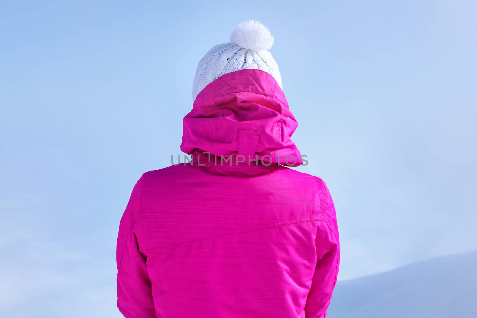 Detail view from back to young woman in pink ski jacket standing on top of the mountain.