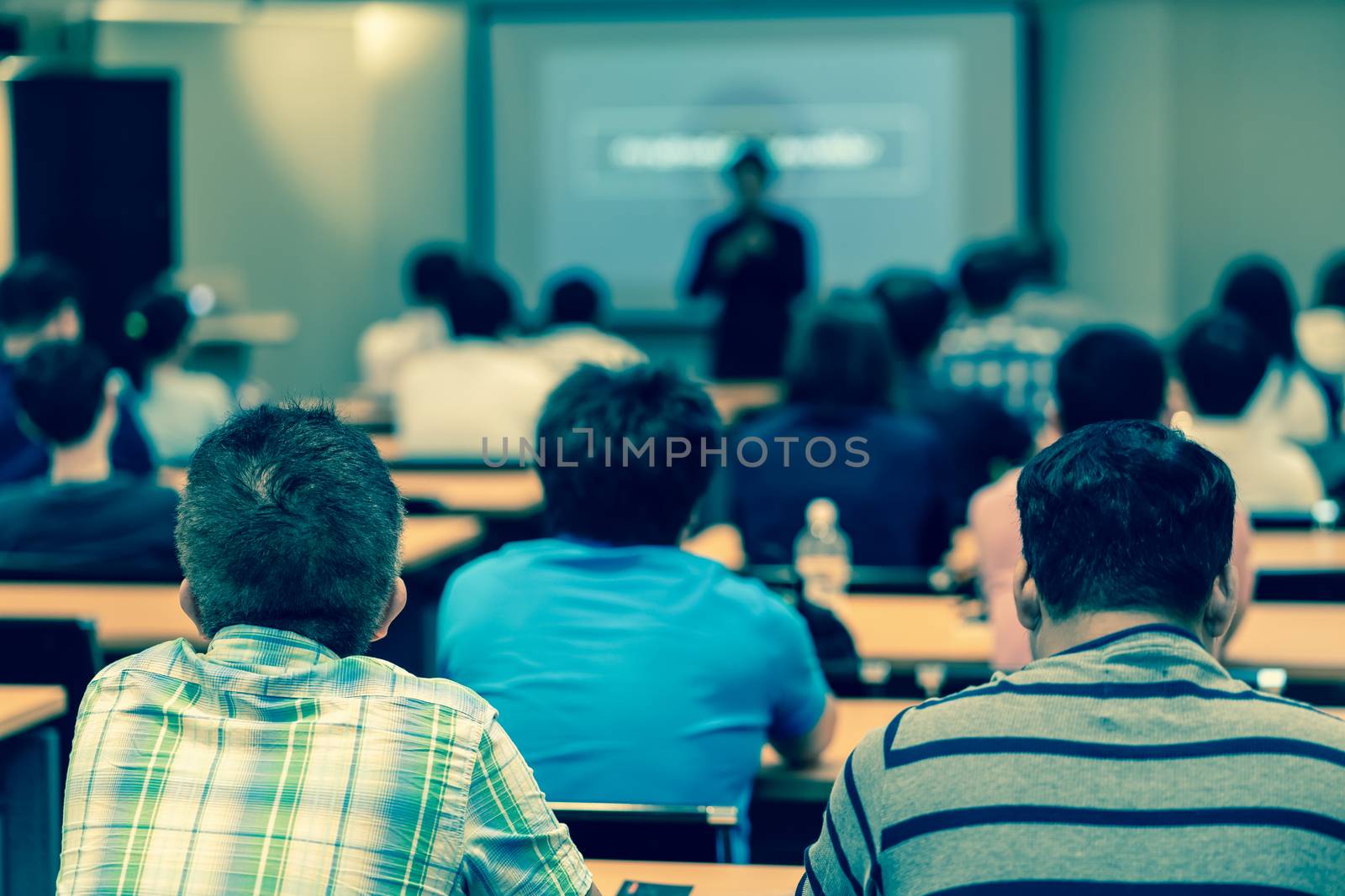 Rear side of Audiences sitting and listening the speackers on the stage in low light meeting room, event and seminar concept