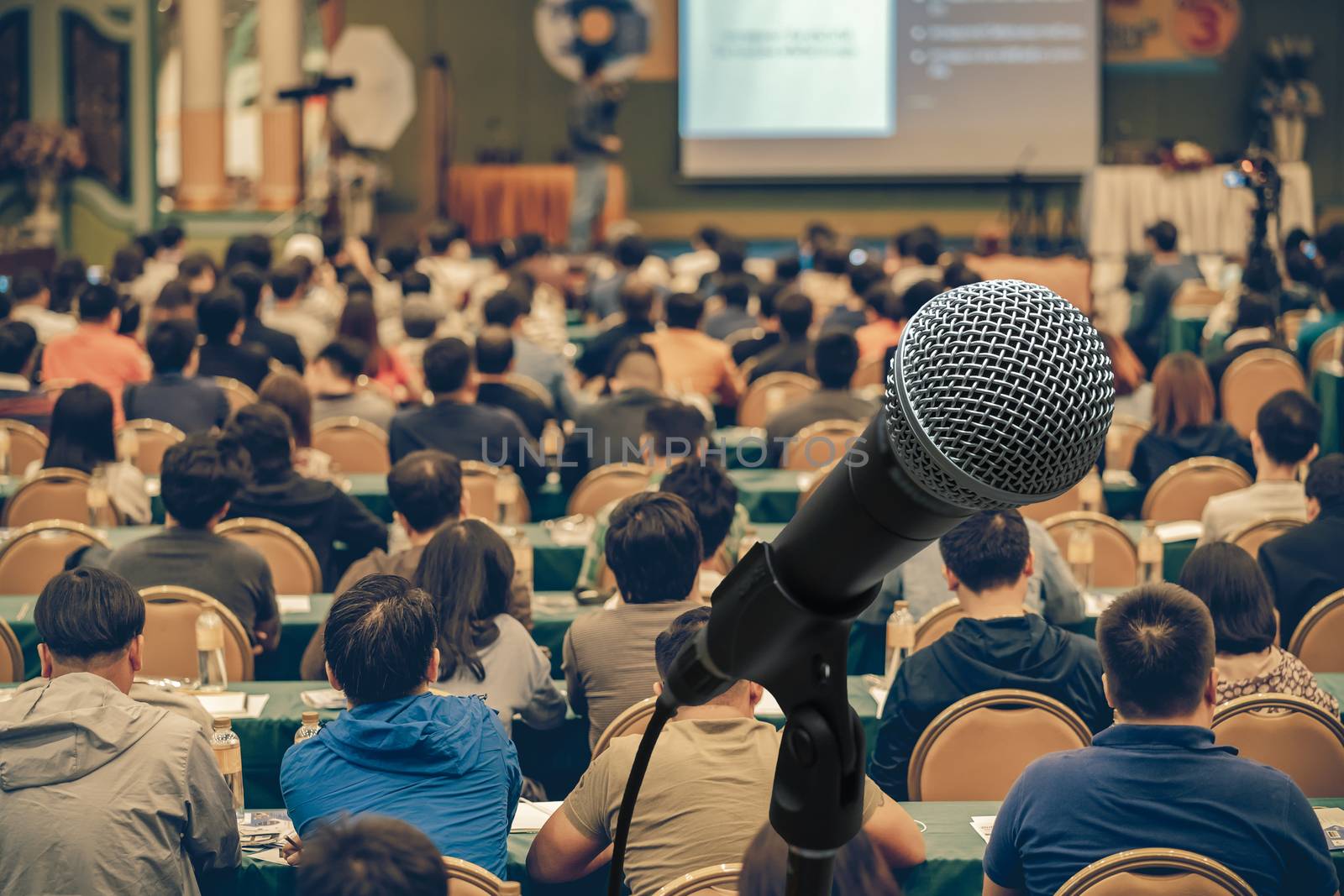 Microphone over Rear view of Audience in the conference hall or seminar meeting which have Speakers are Brainstorming and talking on the stage, business and education about investment concept