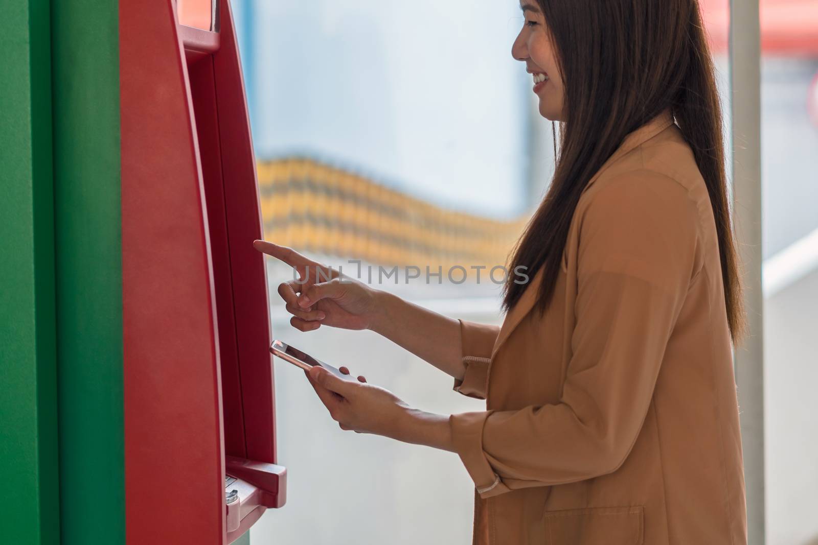 woman using the smart mobile phone for withdrawing in front of the ATM, business Automatic Teller Machine concept