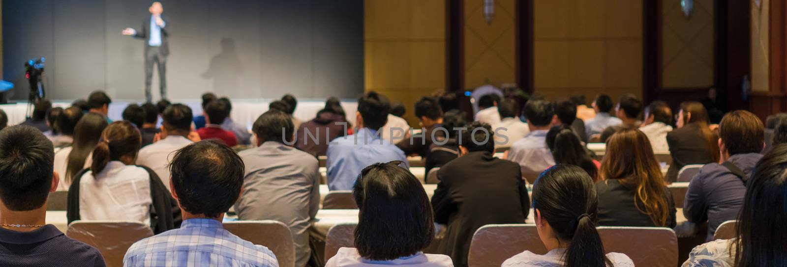 Banner and web page or cover template of Rear side of Audiences sitting and listening the speackers on the stage in low light conference hall, event and seminar concept