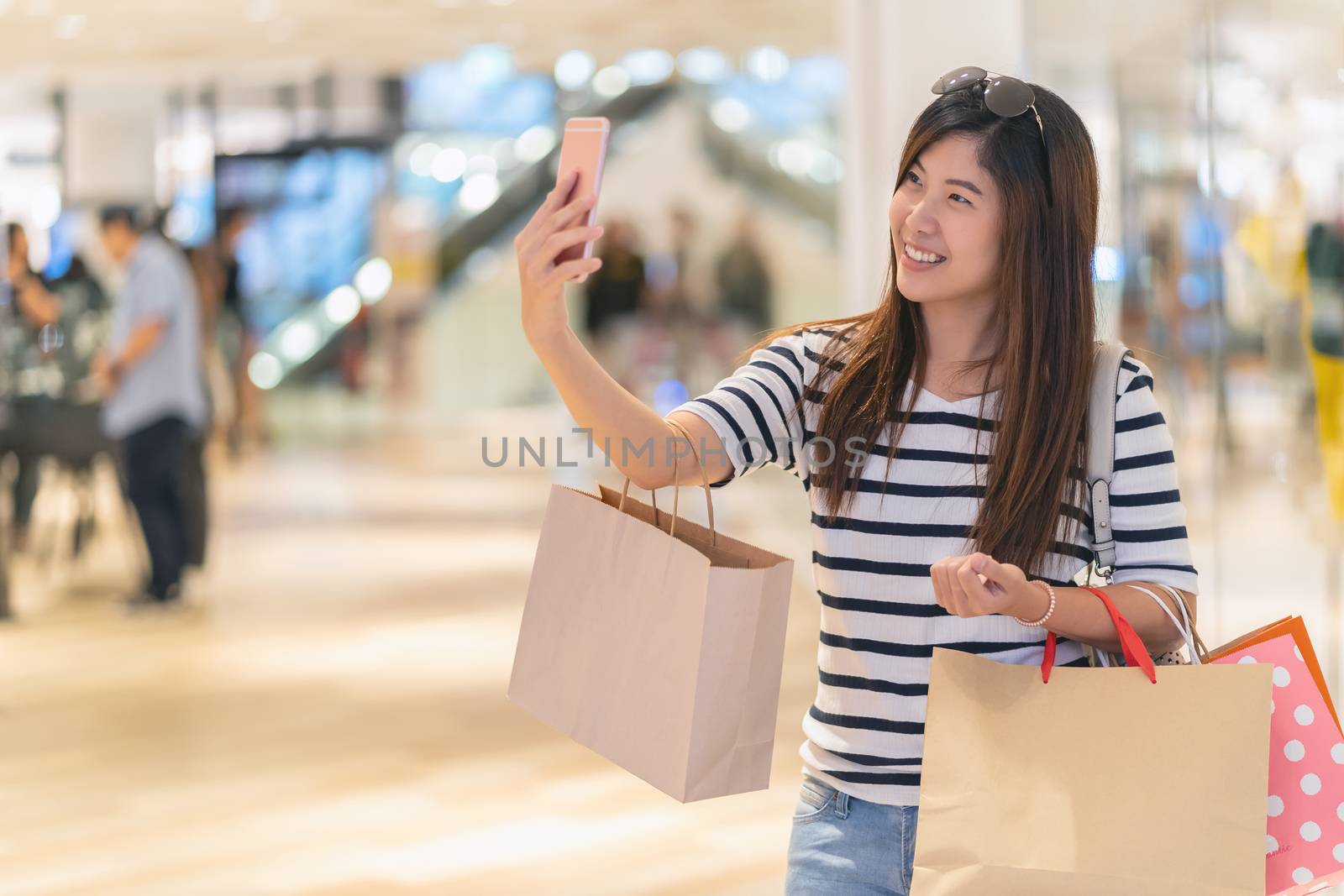Asian woman walking and using the smart mobile phone to selfie with model display mockup with clothes via the glassess in store shop with happy action at department center
