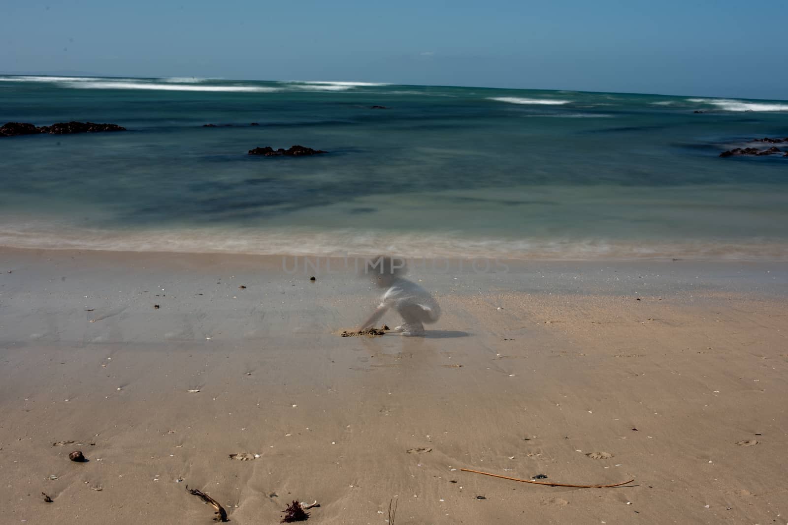 Blurred motion of young child playing at beach with waves in background