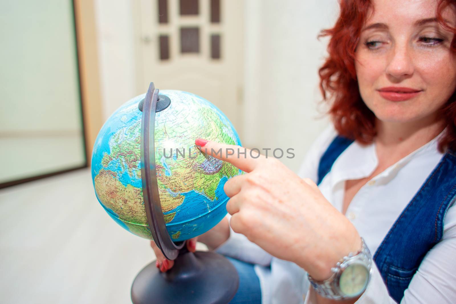 The girl sits on the floor and holds a globe in her hands. Woman points her finger at some place on the globe close-up.