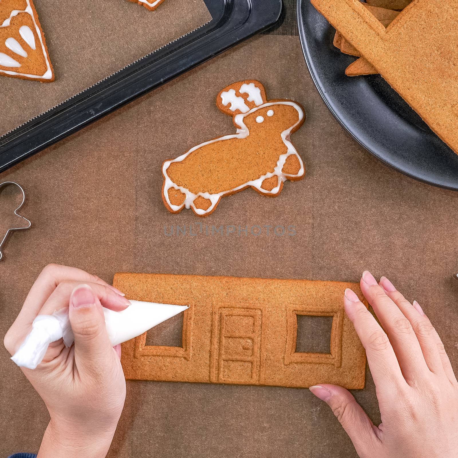 Young woman is decorating Christmas Gingerbread House cookies bi by ROMIXIMAGE