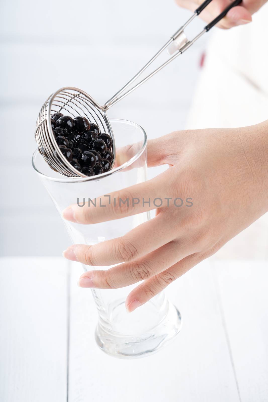 Making bubble tea, scoop and pour cooked brown sugar flavor tapioca pearl bubble balls into cup on white wooden table background, close up, copy space.