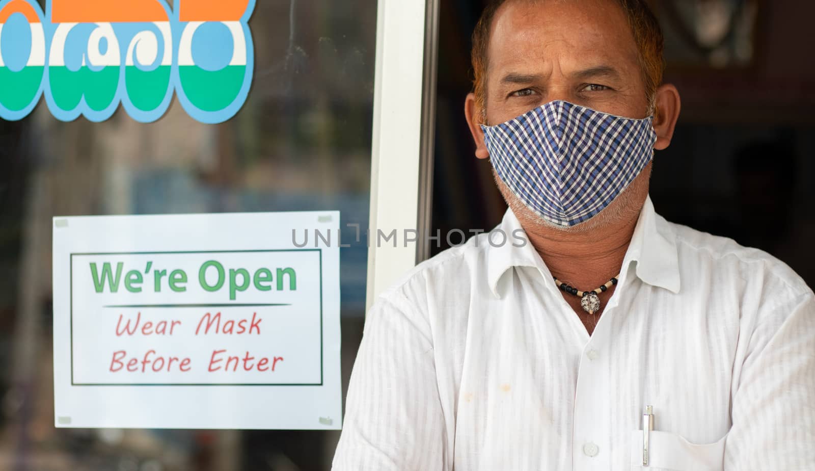 Small business owner in medical mask standing in front of door with we are opn wear mask notice board - concept of support local community during coronavirus or covid-19