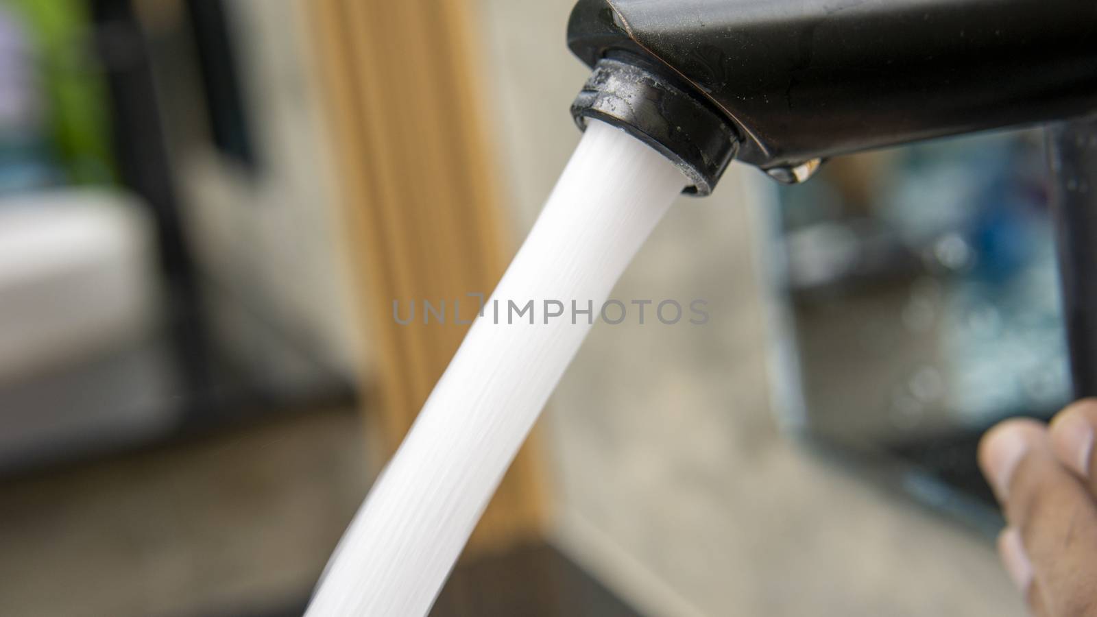 Jet streams of water running from a modern black faucet in the wash basin of outdoor swimming pool area. by sonandonures