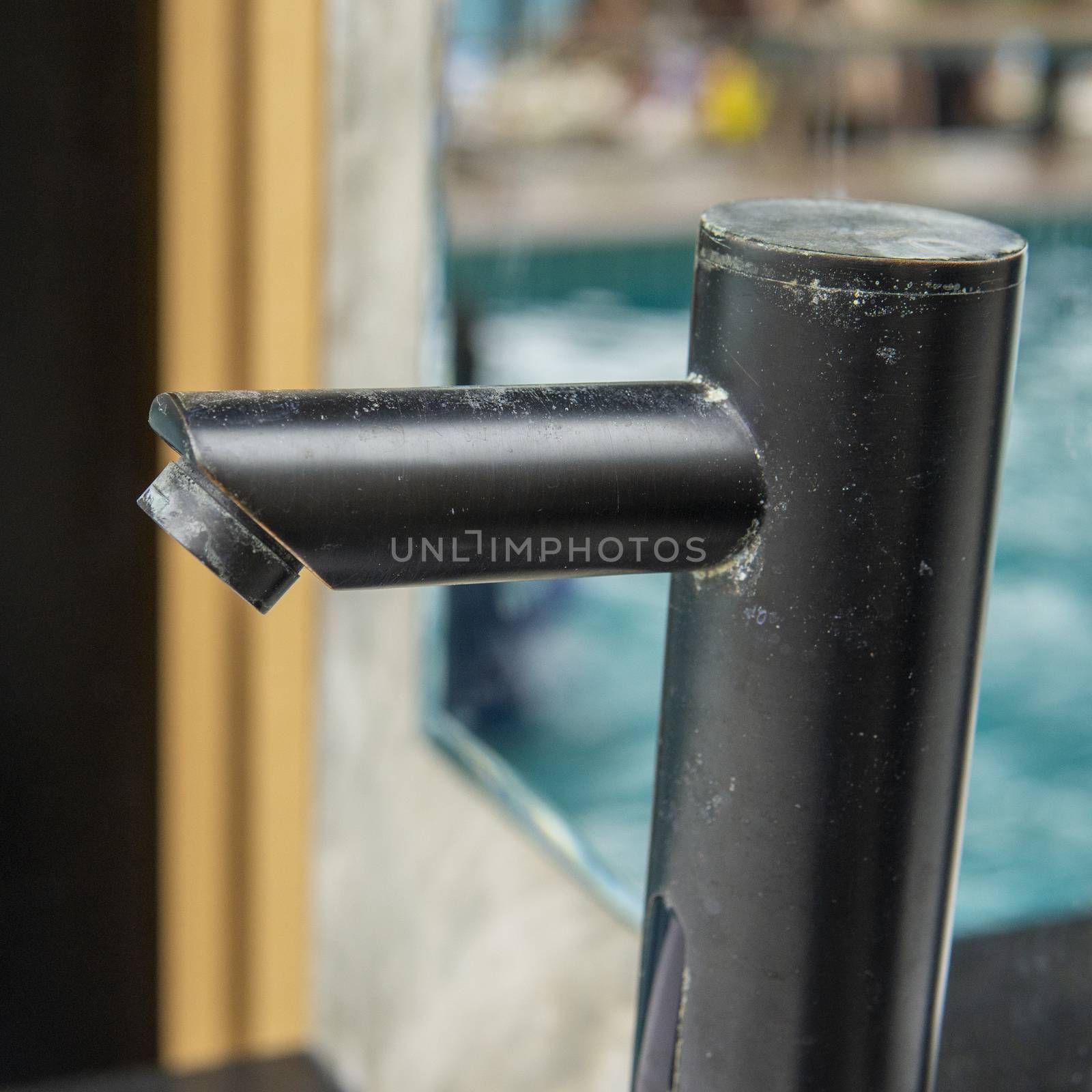 Dust covered modern black color faucet of a wash basin in the outdoor wash area of a swimming pool by sonandonures