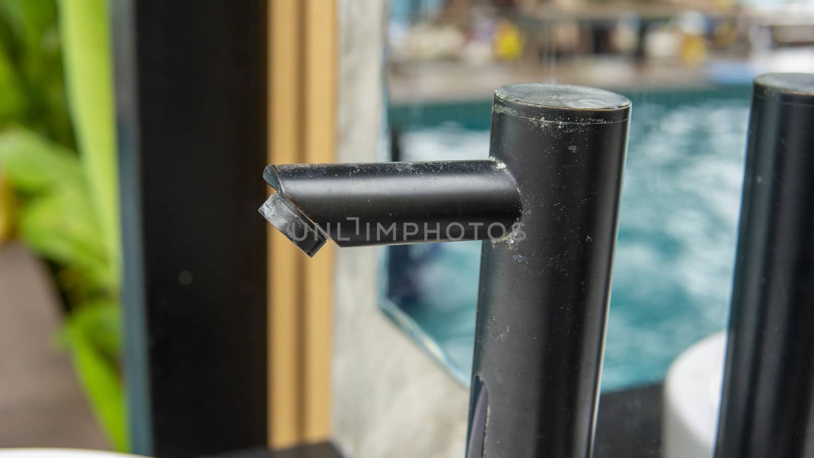 Dust covered modern black color faucet of a wash basin in the outdoor wash area of a swimming pool