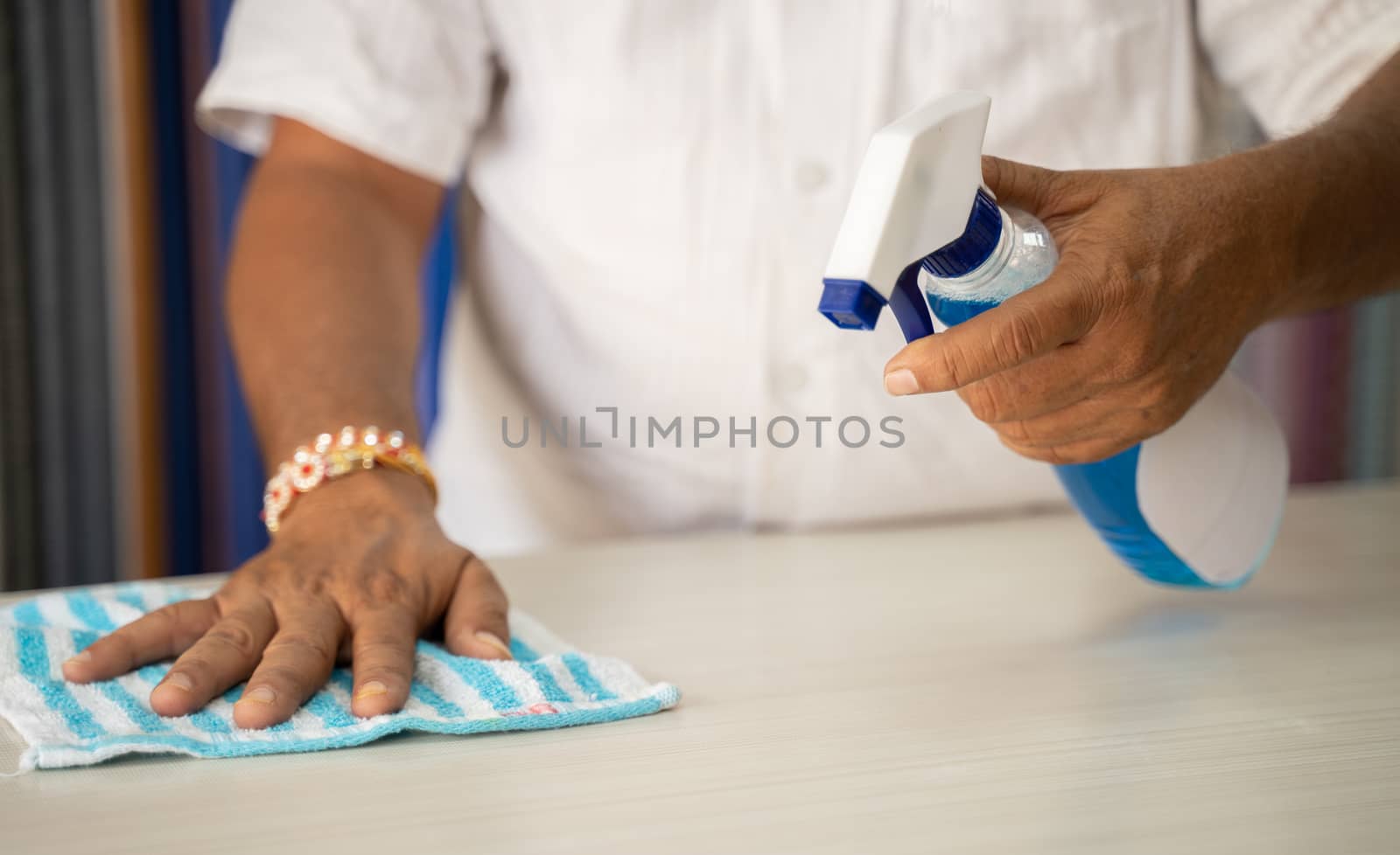 Close up of hands disinfecting table by using sanitizer - Cleaning dust on desk surface with cloth and Disinfectant Spray, to protect from coronavirus or covid-19 infection. by lakshmiprasad.maski@gmai.com