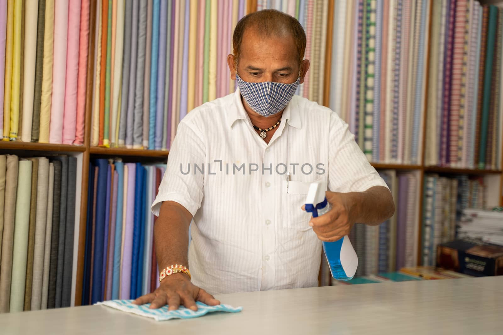 Shopkeeper in medical mask disinfecting table by using sanitizer - Cleaning dust on desk surface with cloth or Disinfectant Spray, to protect from coronavirus or covid-19 infection