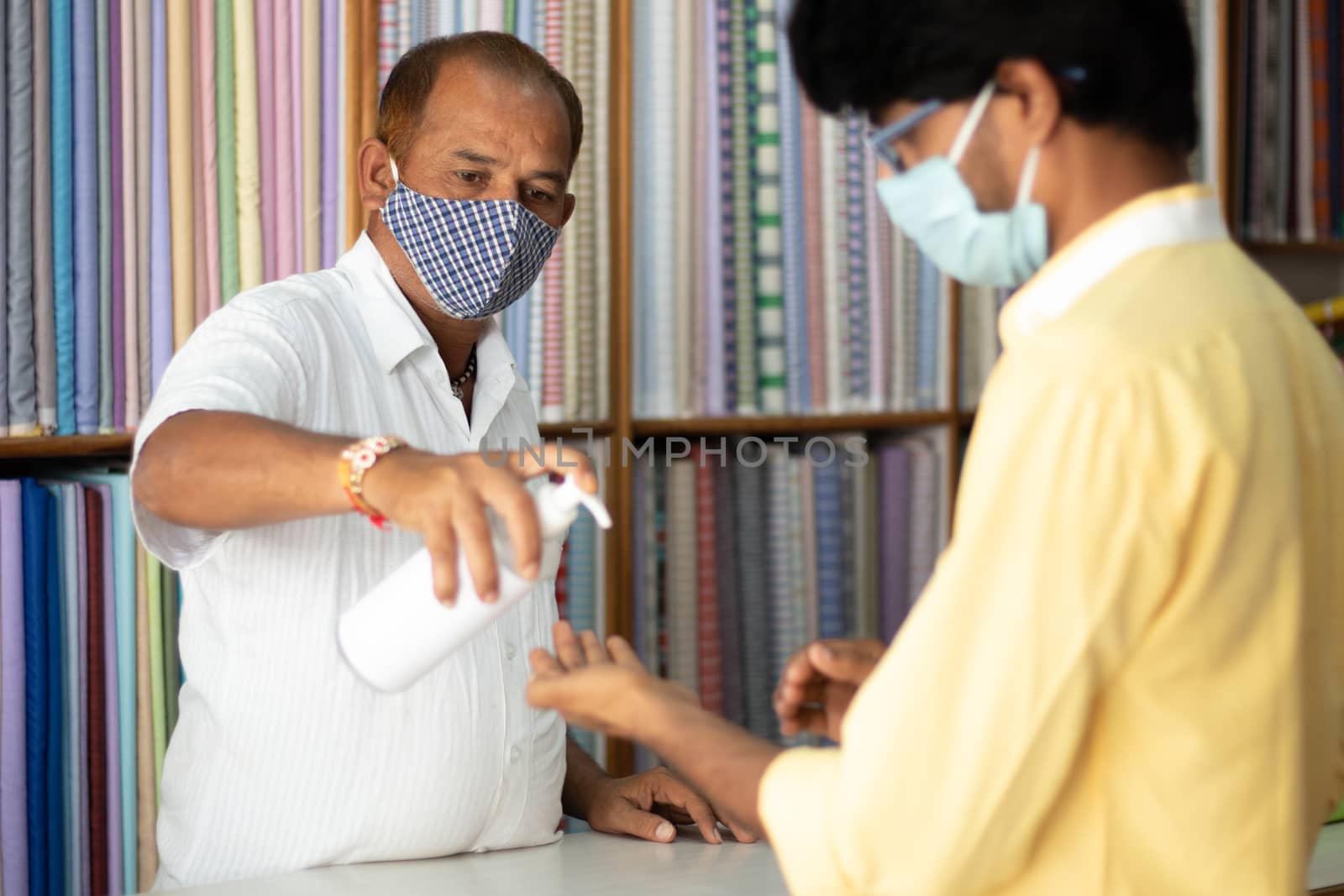 Shopkeeper giving Hand sanitizer to customer to stop spreading coronavirus or covid-19 infection - concept of safety, hygiene measures at business and workplace. by lakshmiprasad.maski@gmai.com