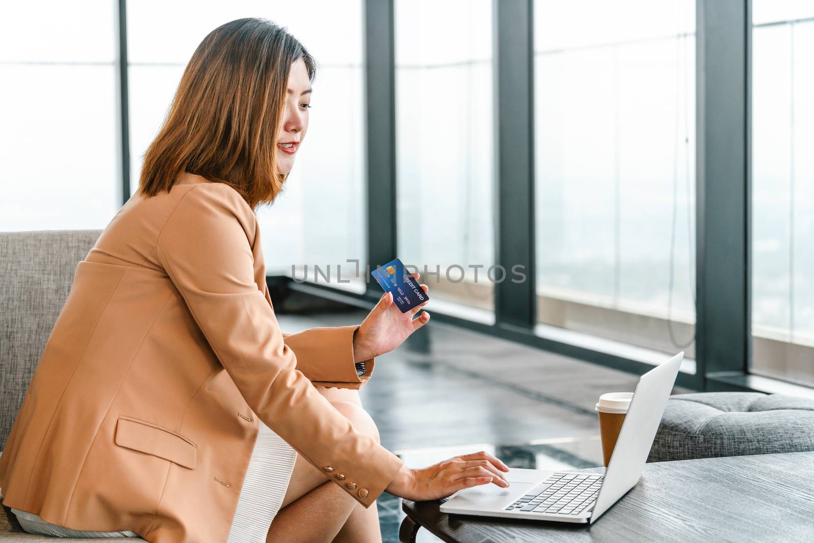 Portrait Asian woman using credit card with mobile phone, laptop for online shopping in modern lobby or working space, coffee cup, technology money wallet and online payment concept,credit card mockup