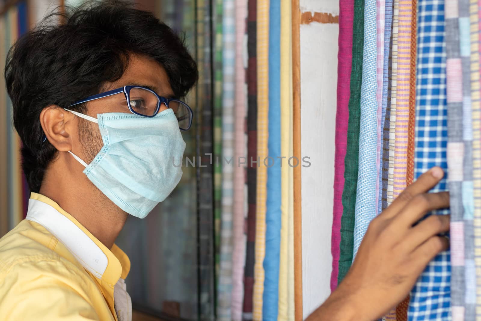 Young man with medical mask selecting or buying cloth at store during coronavirus or covid-19 pandemic - Concept of new normal, business reopen and support local community after lock down. by lakshmiprasad.maski@gmai.com