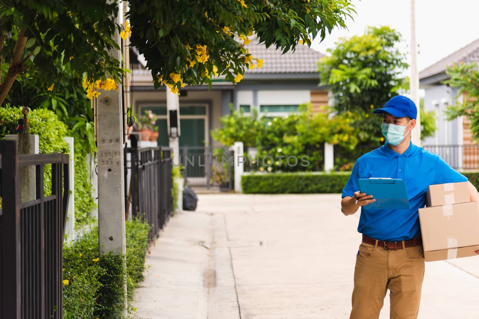 Asian young delivery man courier hold parcel post boxes he protective face mask service and walk looking for customer home location, under curfew pandemic coronavirus COVID-19