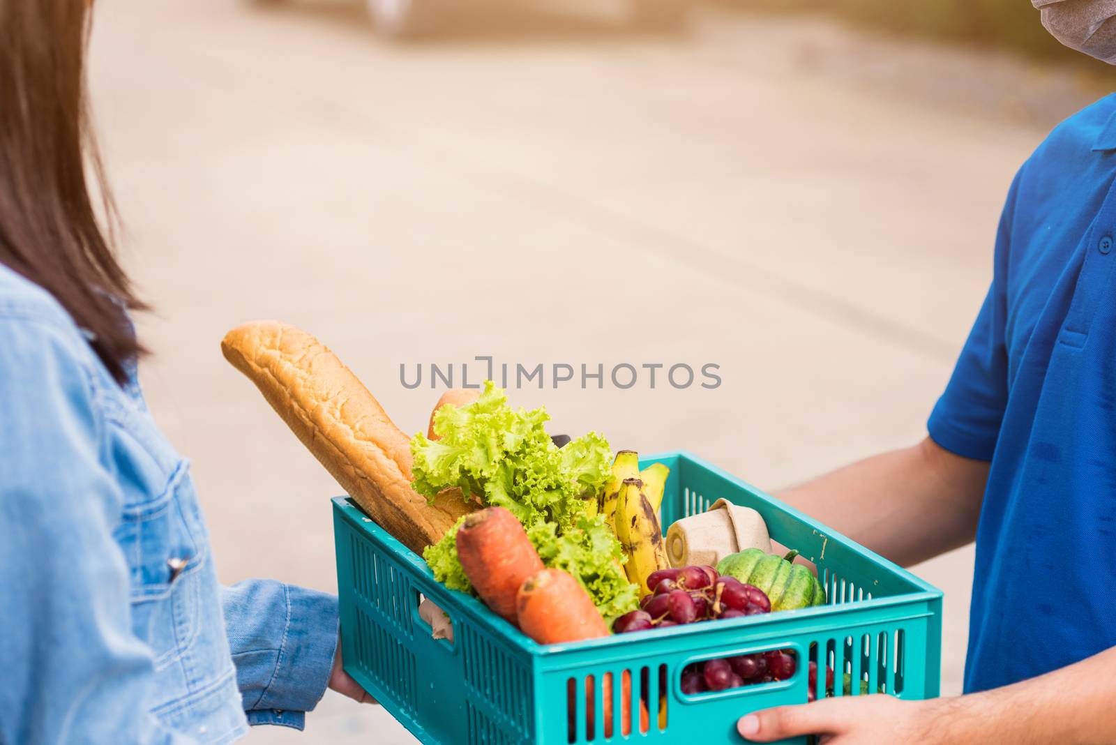 Asian young delivery man wear face mask making grocery fast service giving fresh food vegetable in plastic basket to woman customer receive at house door after pandemic coronavirus, Back to new normal