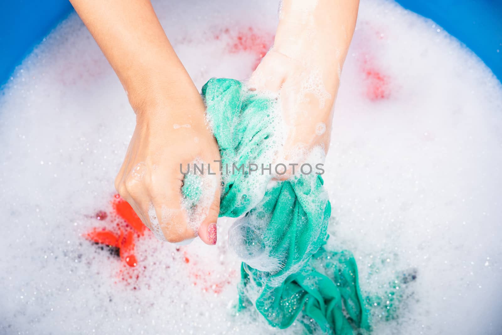 Closeup young Asian woman use hands washing color clothes in basin with detergent have soapy bubble water, studio shot background, laundry concept