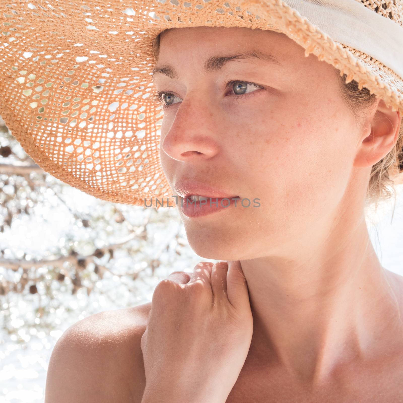 Close up portrait of no makeup natural beautiful sensual woman wearing straw sun hat on the beach in shade of a pine tree.