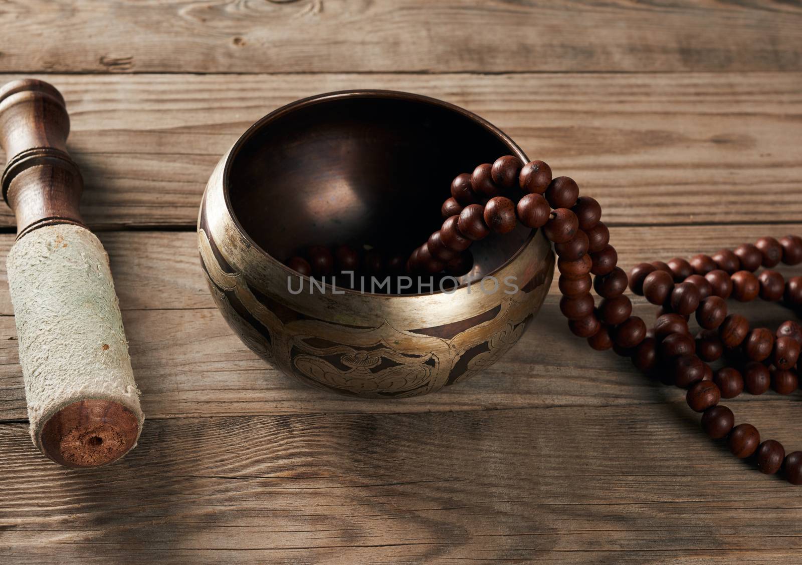 Tibetan singing copper bowl with a wooden clapper on a brown wooden table, close up