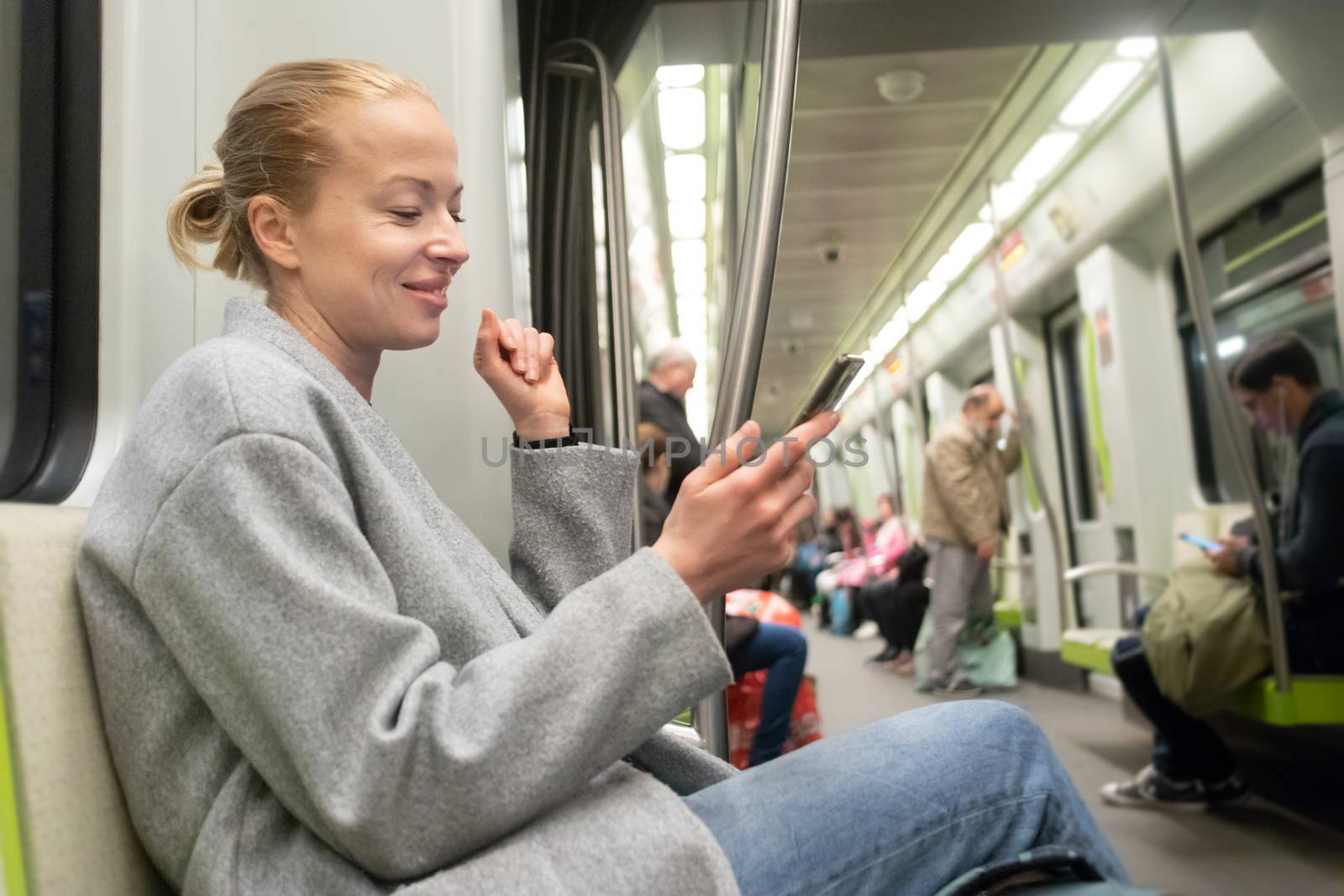 Portrait of lovely girl typing message on mobile phone in almost empty public subway train. Staying at home and social distancing recomented due to corona virus pandemic outbreak.