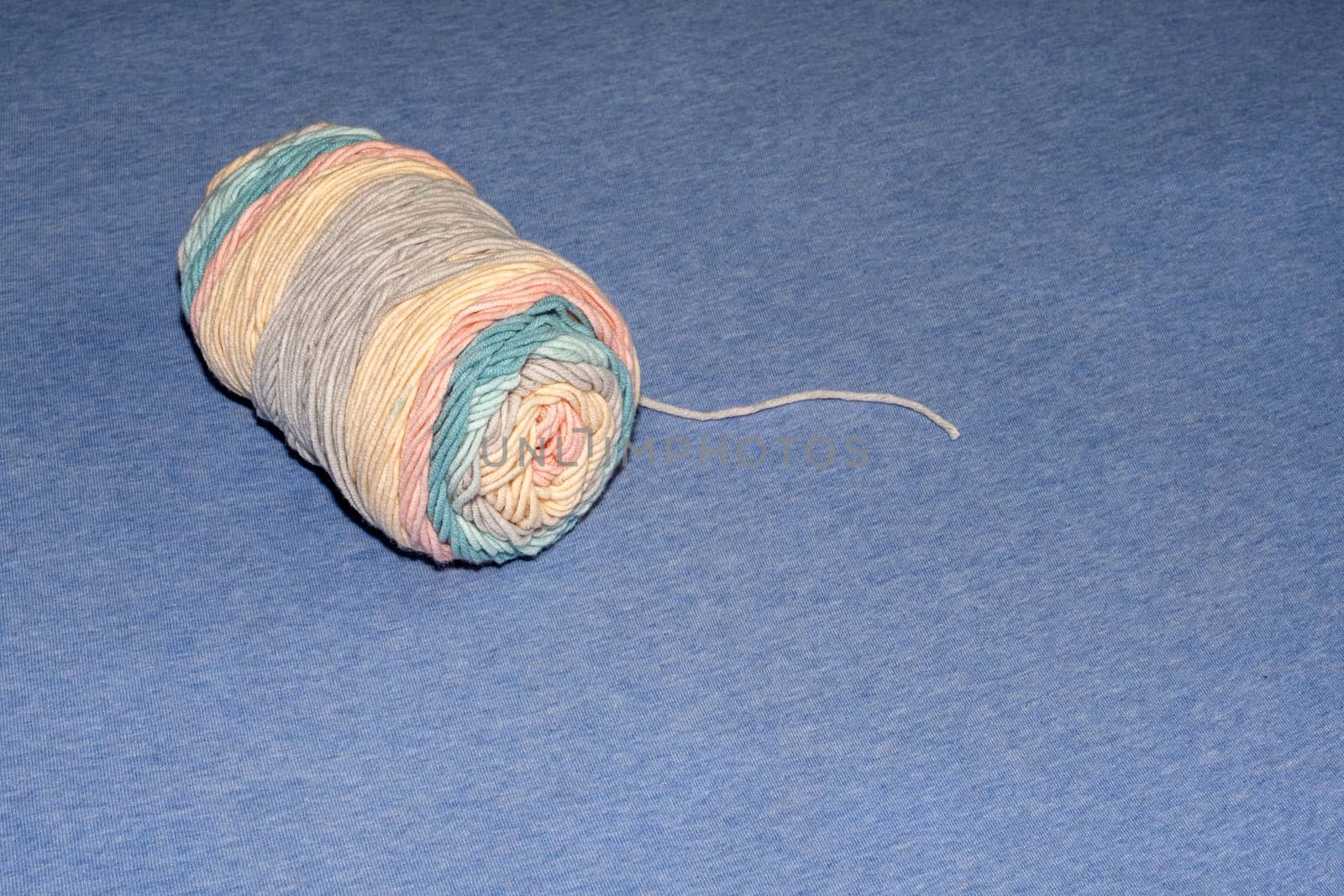 A tightly-wrapped skein of yarn has pastel blue, pink and orange colors. The yarn lies on a fabric surface, with a single thread extending outwards.