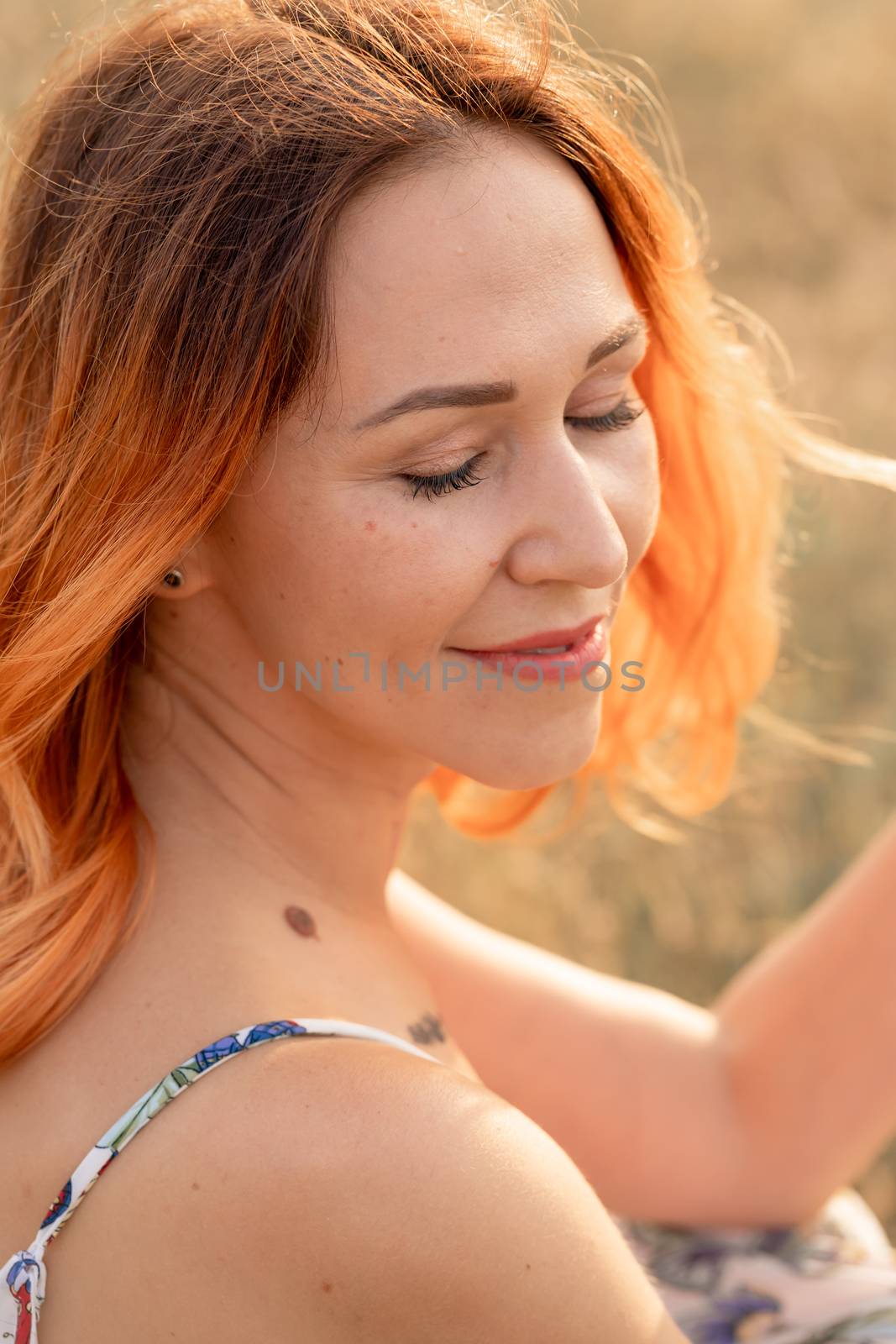 Tender beautiful red-haired girl enjoys the sunset in a field with a hill