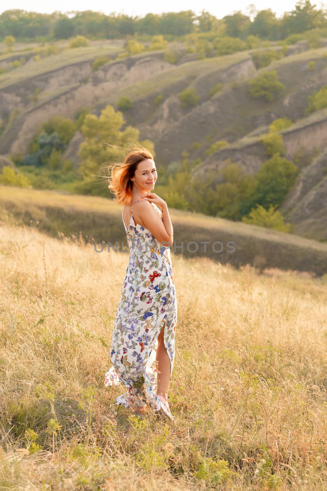 Beautiful red-haired girl is having fun and dancing in a field at sunset.