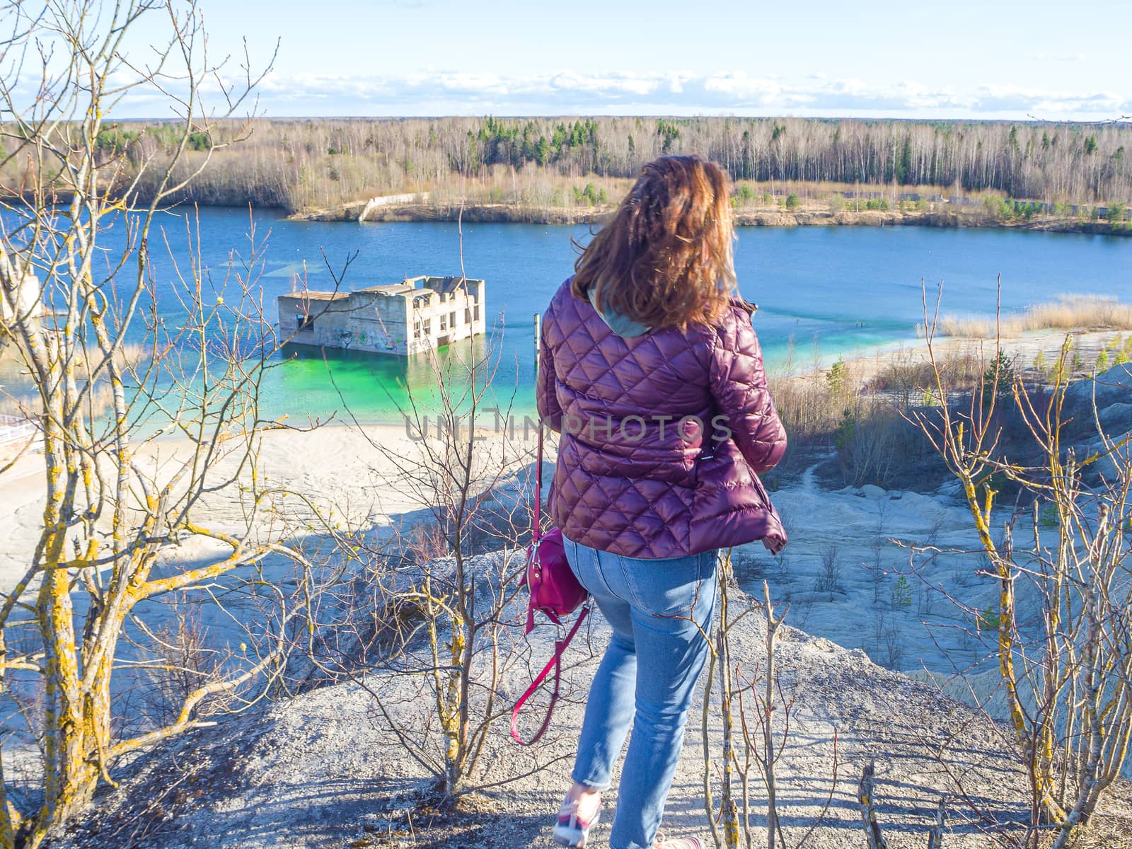 Hiker on mountain top. Woman is standing with an Abandoned Quarry and water on the background. Scenic View Of Land Against Clear Blue Sky. Panoramic View.