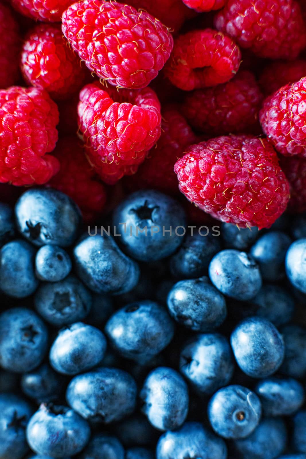 A close-up of raspberries and black blueberry split the frame. Summer vitamins.