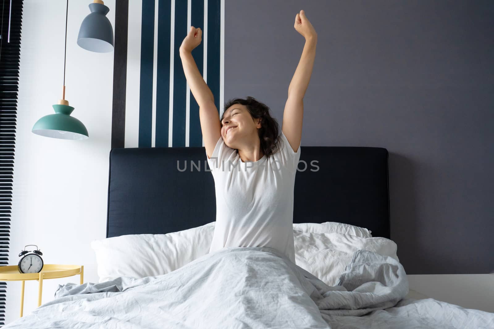 Beautiful girl wakes up in a good mood in a stylish apartment. Stretches with a smile starting the day.