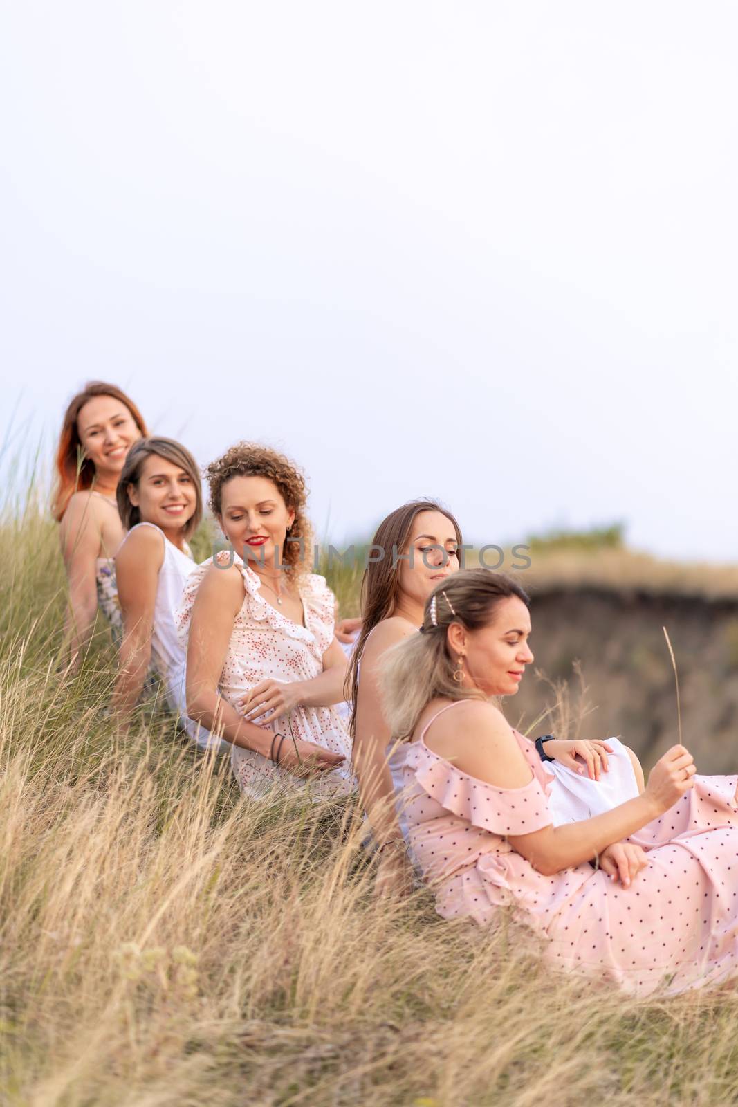 A cheerful company of beautiful girls friends enjoy a picturesque panorama of the green hills at sunset.