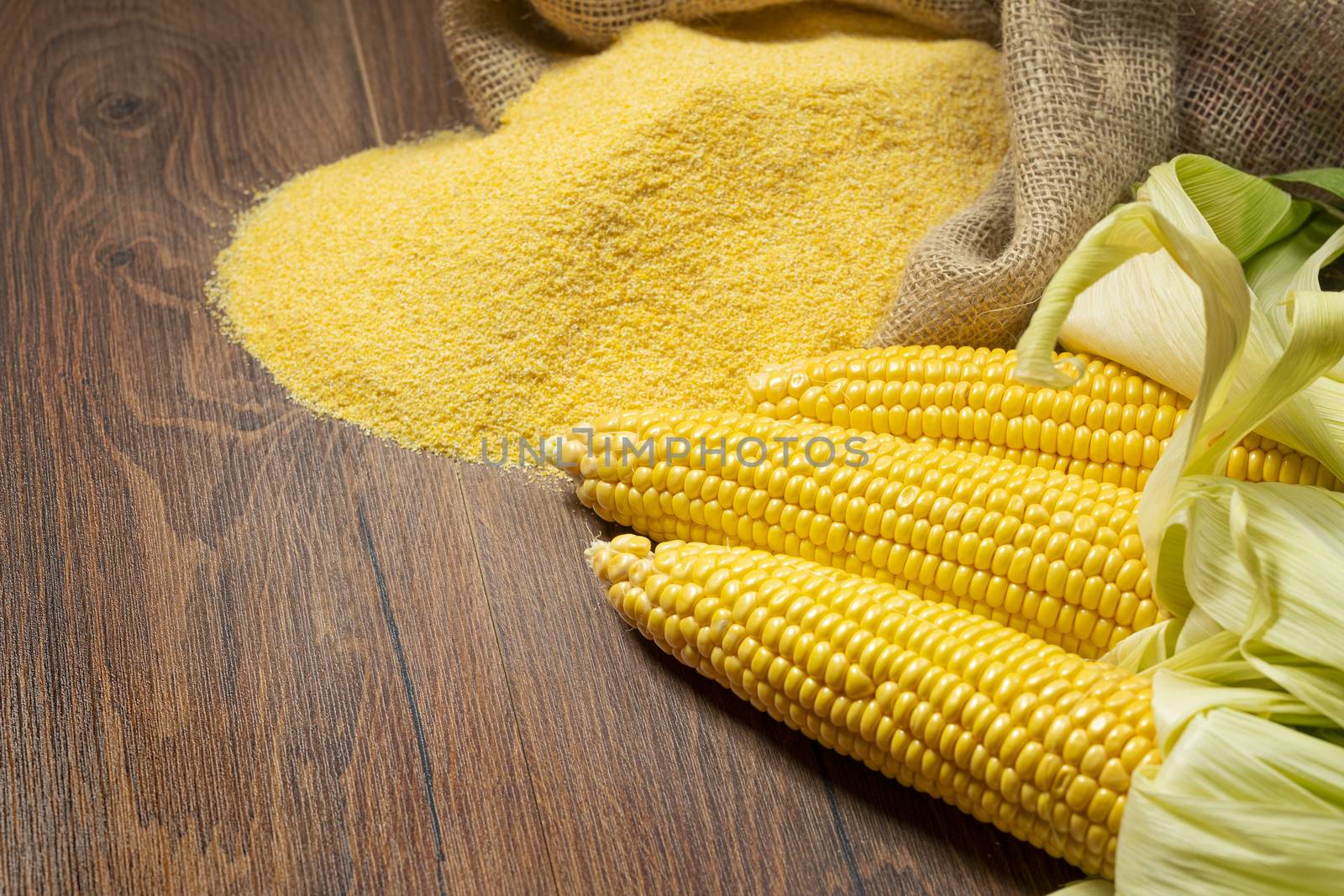 Ripe young sweet corn cob,on left stack cornmeal on wooden background, copy space.Gluten free food concept