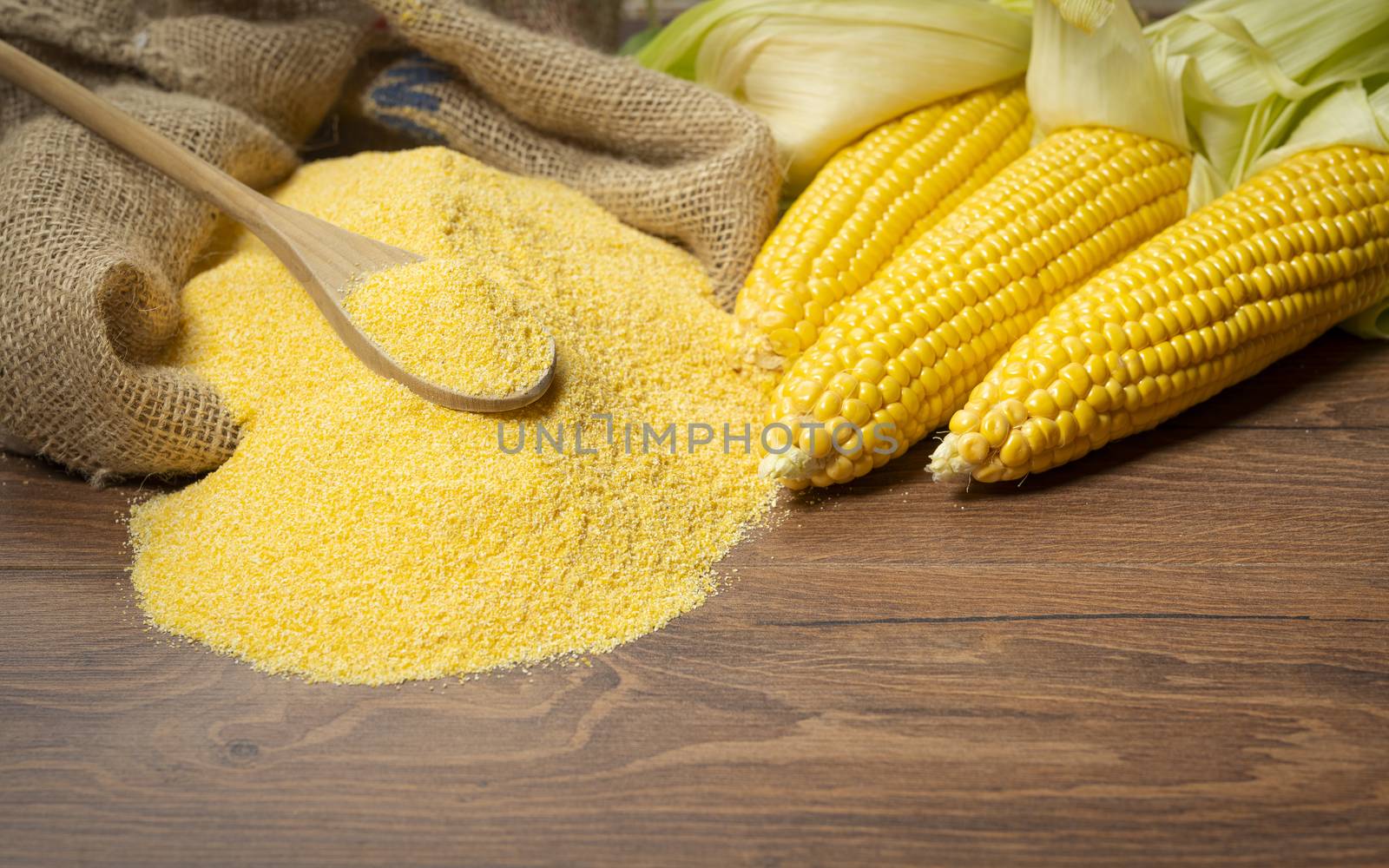 Ripe young sweet corn cob,on left stack cornmeal and spoon on top,wooden background, copy space.Gluten free food concept