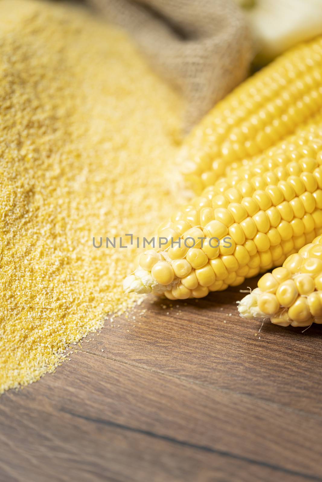 Ripe young sweet corn cob,on left stack cornmeal on wooden background, close up.Gluten free food concept