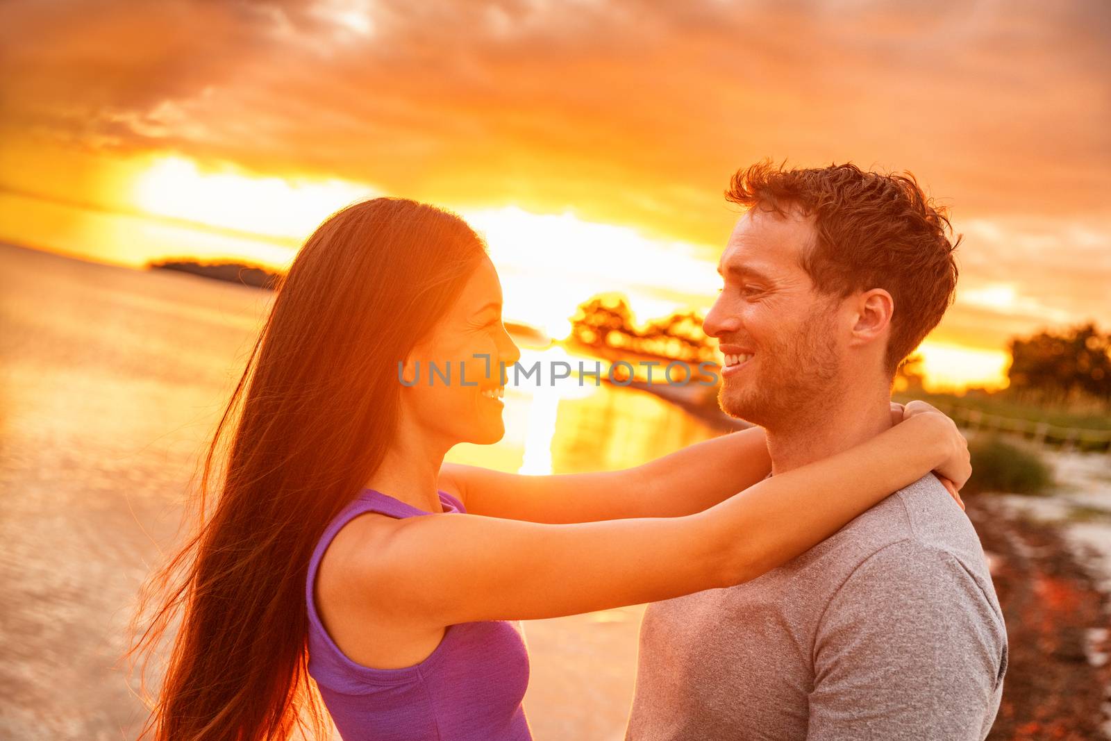 Couple in love laughing at sunset glow on summer beach tropical Caribbean vacation. Happy Asian woman smiling at Caucasian man by Maridav