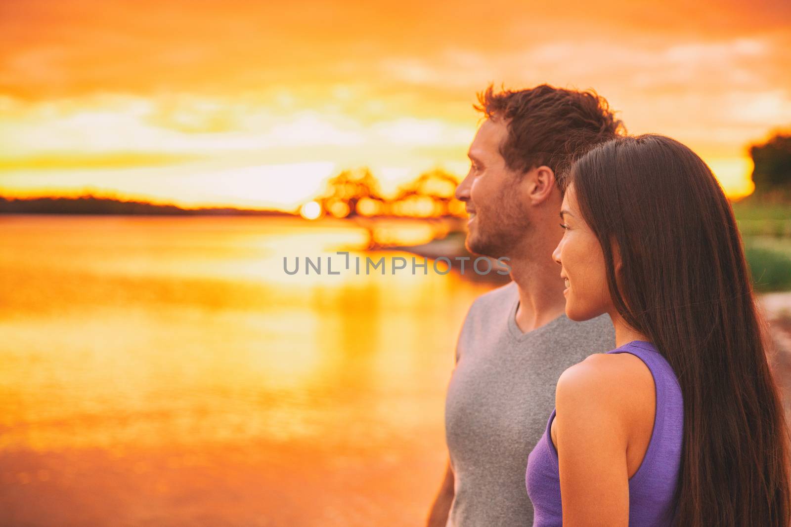 Couple relaxing on beach watching sunset glow over ocean in Caribbean background. Asian girl, Caucasian man interracial relationship.