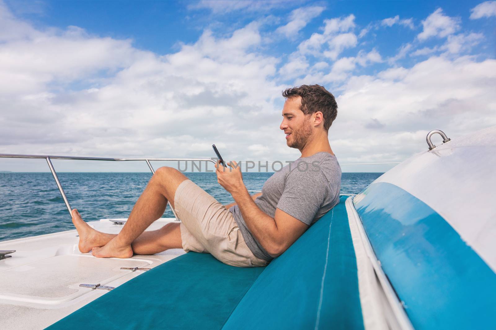 Boat man using mobile phone texting on satellite internet while relaxing on deck of yacht luxury lifestyle by Maridav