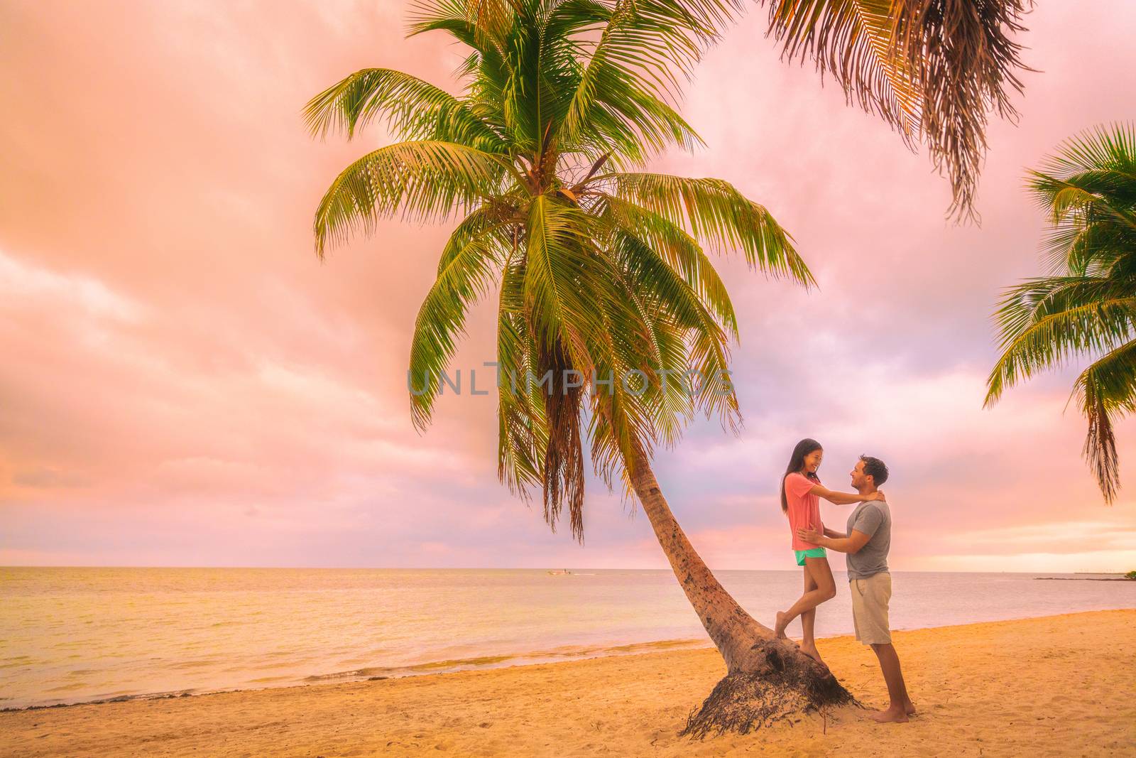 Romantic sunset stroll young couple in love embracing on palm trees at pink dusk clouds sky. Romance on summer travel vacation.