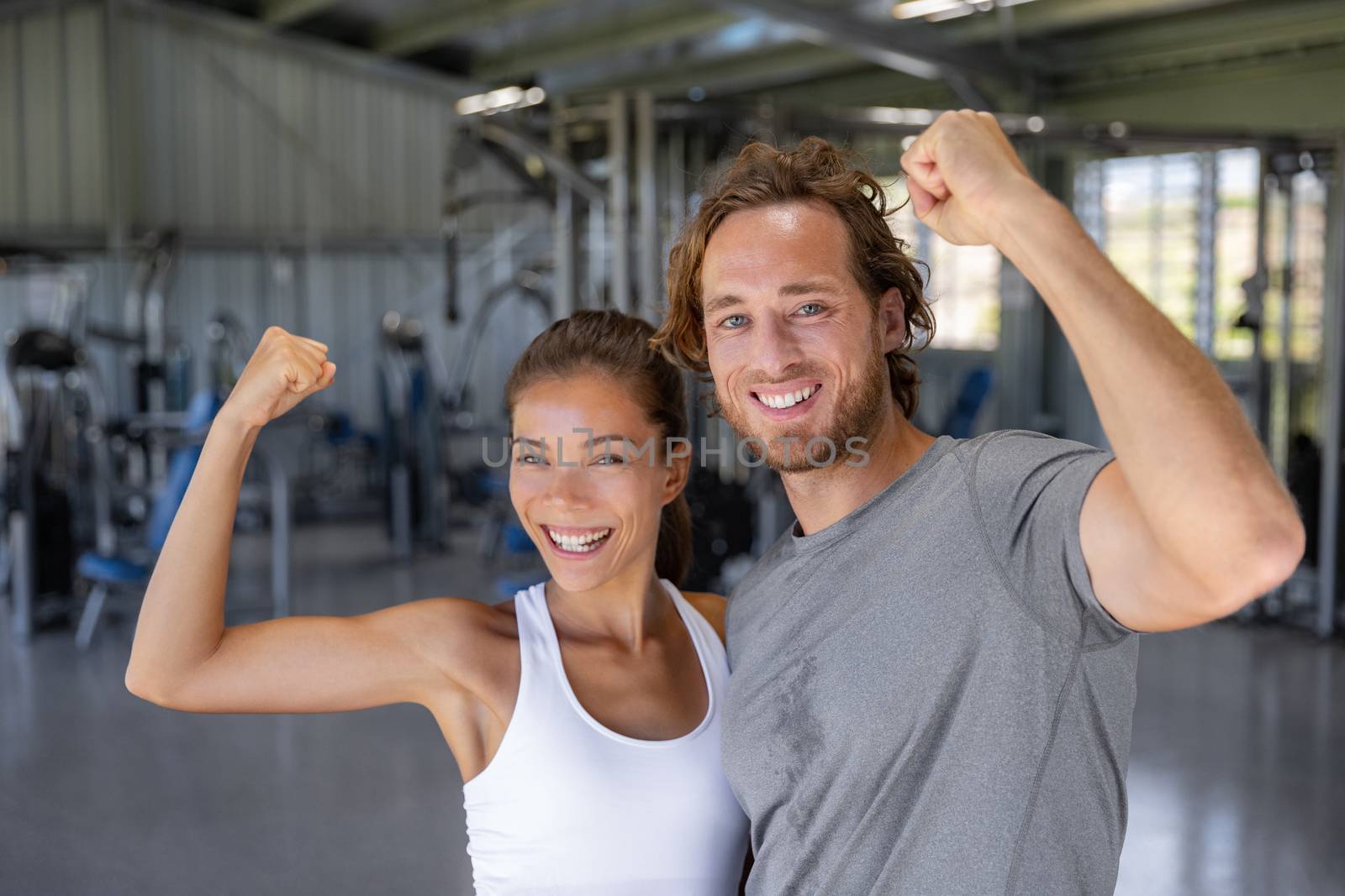 Fit power couple happy flexing strong arms showing off success training at fitness gym - Smiling Asian woman, Caucasian man .