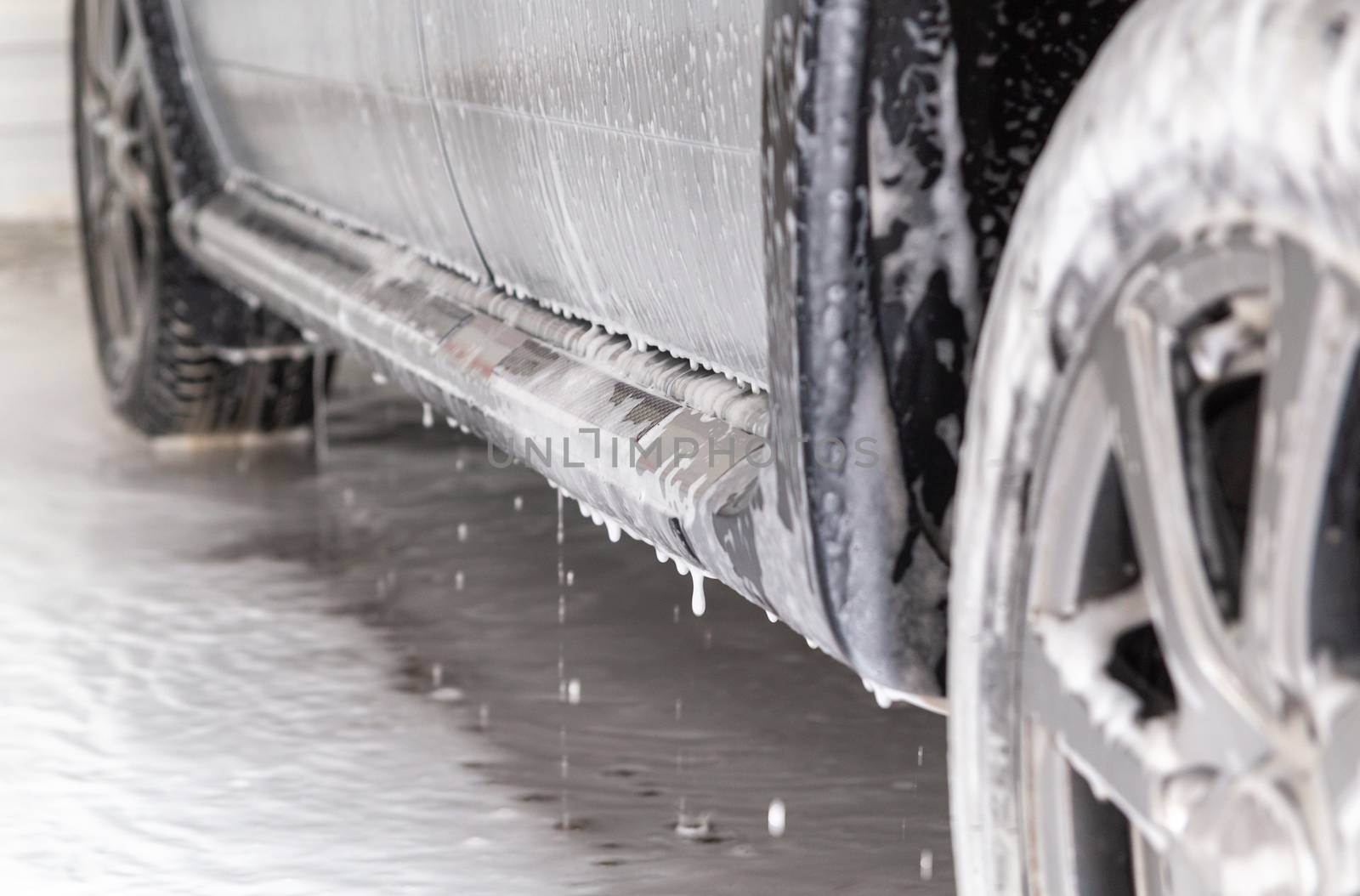 close-up view of silver car step at carwash with soap sud smudges and drops.