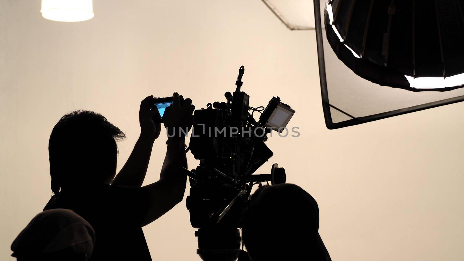 Silhouette of photographer checking for movie camera and set before shooting in studio.